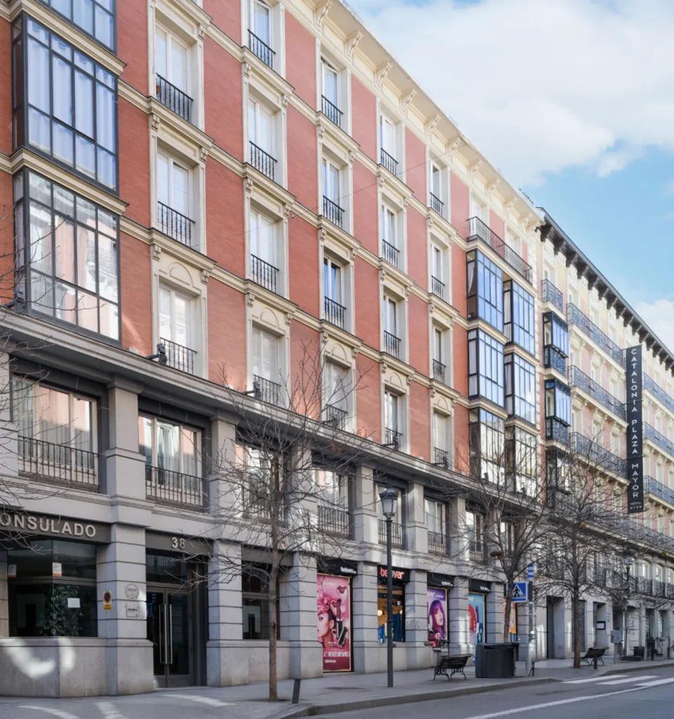 Vista de una calle de la ciudad con edificios históricos de varias plantas, grandes ventanales y balcones. Un paseo amplio con tiendas y establecimientos.