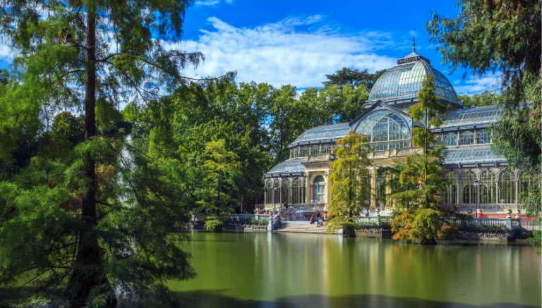 alt="Palacio de Cristal en el Parque del Retiro rodeado de vegetación, Madrid"
