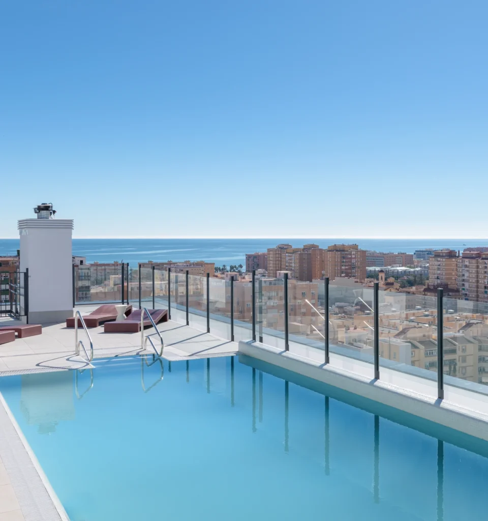 Piscina exterior en la azotea, barandilla de seguridad de cristal, escalera metálica y vistas a la ciudad.