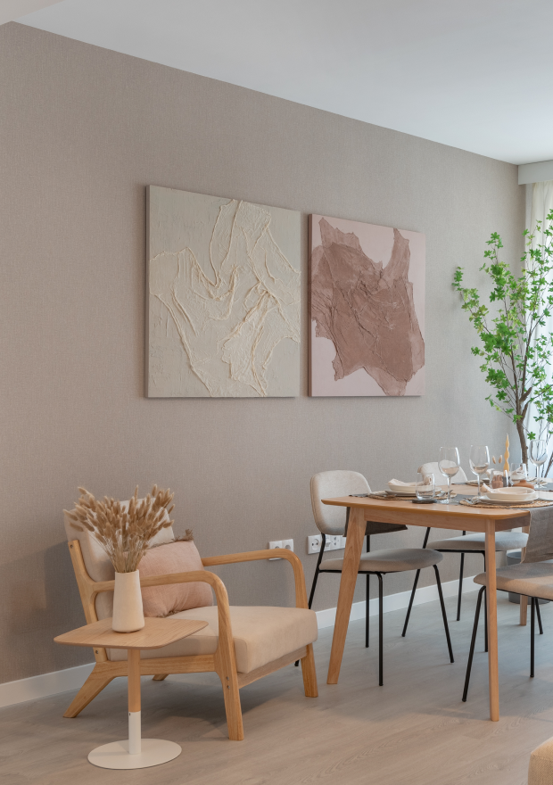 Un comedor moderno con una mesa de madera para seis comensales, sillas beige, cuadros decorativos, un acogedor sillón individual, plantas en macetas y luz natural.